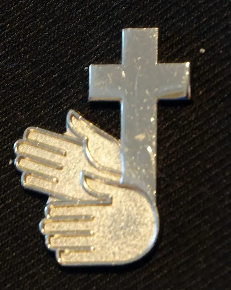 Zwei Hände, aus denen das Kreuz wächst: Anstecker am Sakko von Gehörlosenpfarrerin Daniela Milz-Ramming.