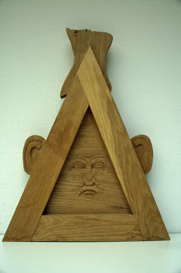 Holzskulptur aus einem Dreieck mit Gesicht und Ohren, sowie einem Gesicht an der Spitze, das hilfesuchend zu Gott aufblickt