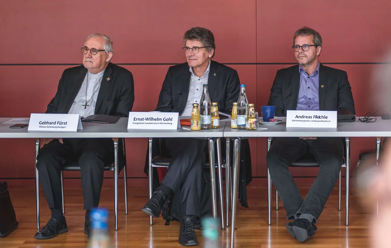 Landesbischof Ernst-Wilhelm Gohl (Mitte) sitzt neben Dr. Gebhard Fürst, Bischof der Diözese Rottenburg-Stuttgart (links), und Andreas Felchle, Vizepräsident des Landessportverbands (rechts).