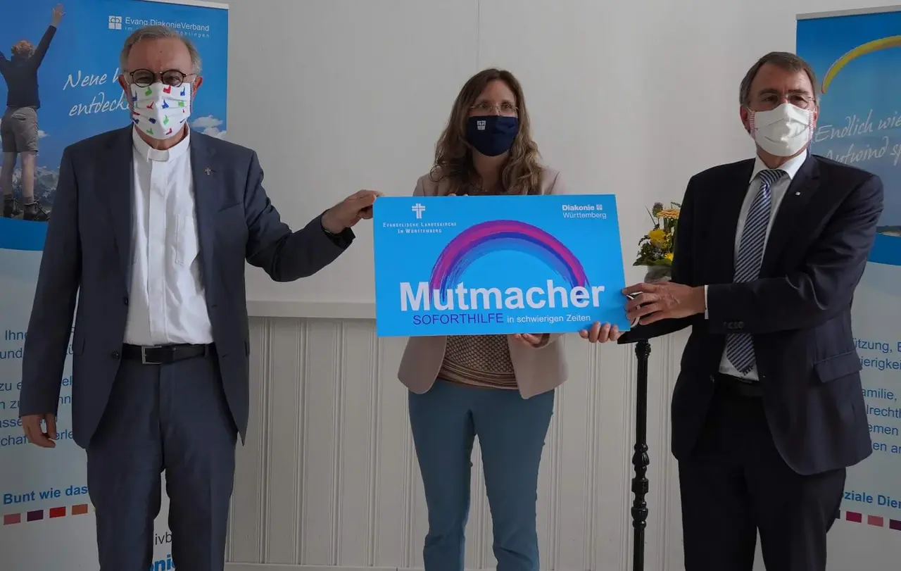 Landesbischof Frank-Otfried July (links) und Diakonie-Vorstandvorsitzender Dieter Kaufmann (rechts) überreichen einen symbolischen Mutmacher an Simone Schächterle vom Diakonieverband Böblingen.