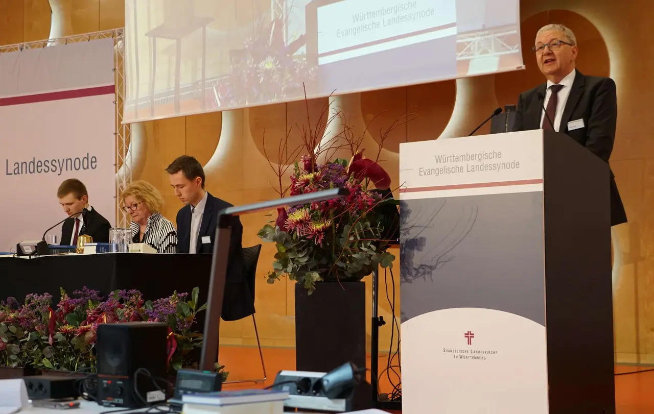 Dekan i. R. Hellger Koepff (OK) hat als Vorsitzender des Nominierungsausschusses die Wahlvorschläge eingebracht. Im Hintergrund Alterspräsidentin Hannelore Jessen (OK) mit den kommissarischen Schriftführern Michael Klein (LG, links) und Christoph Lehmann (LG).